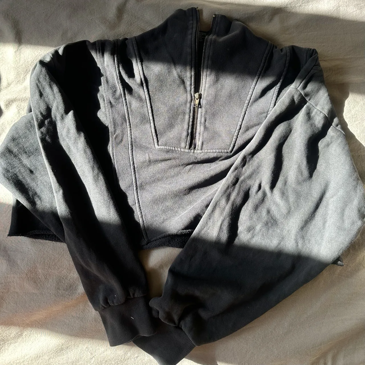 Buzo crop negro con cierre al cuello y mangas largas. Posee puños y cintura elastizados.