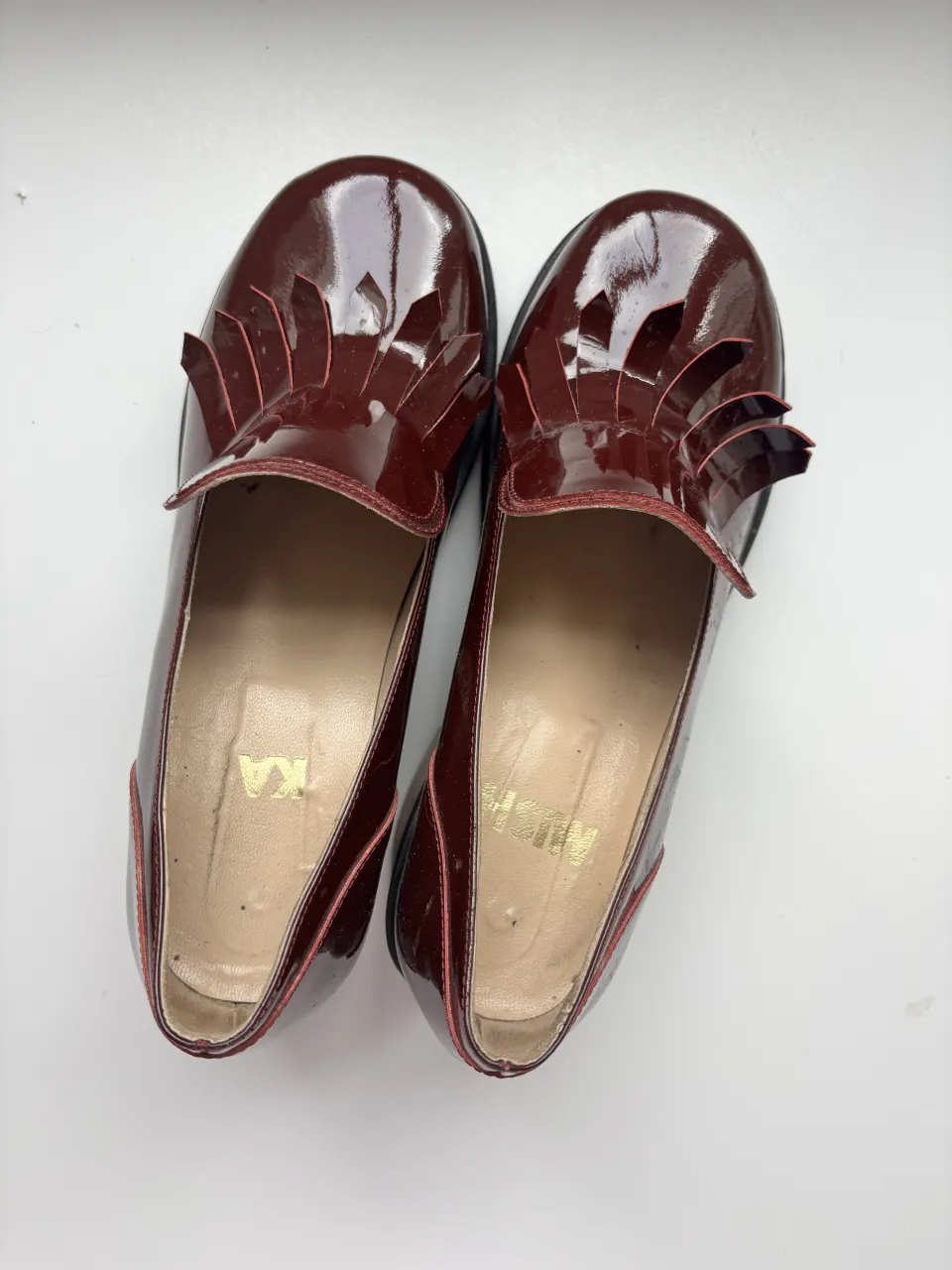 Zapatos de charol color bordó con detalle de flecos en la capellada y taco de madera. La suela es de goma.