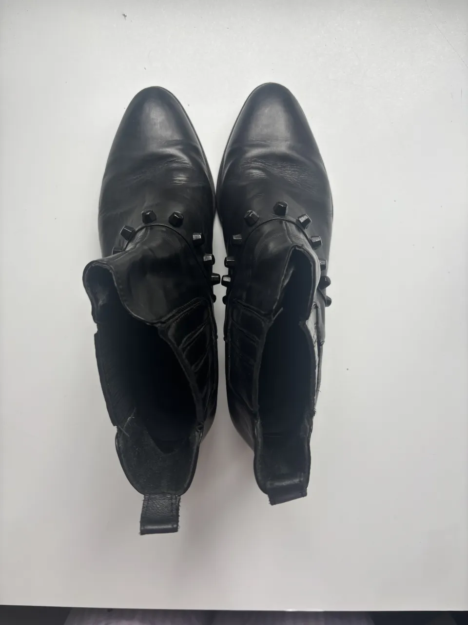 Botas negras Sarkany, de cuero con tachas alrededor del cuello y en la parte trasera. Tienen elástico a los costados y un pequeño tirador en la parte trasera superior. Taco cuadrado.