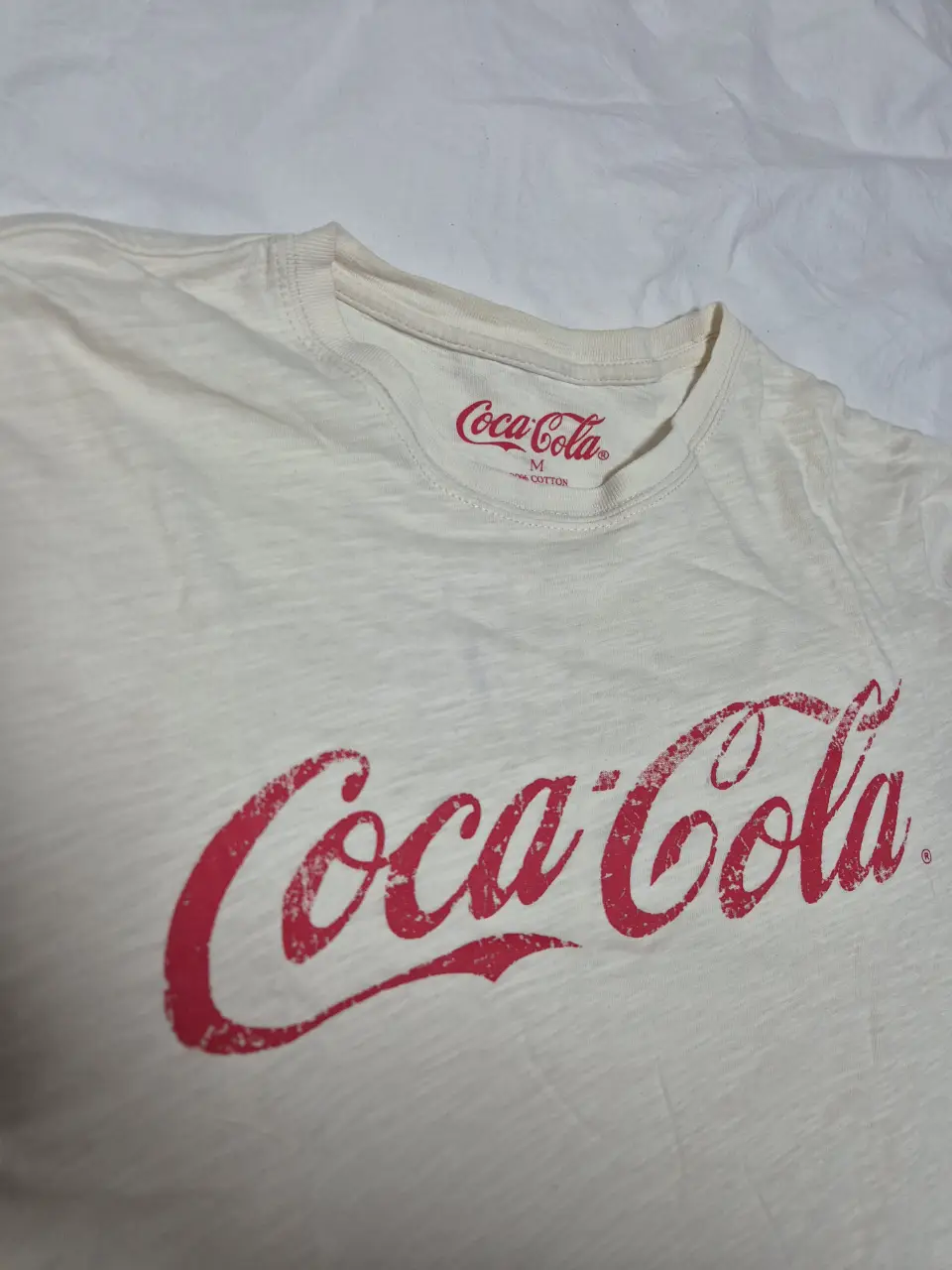 Remera de algodón color crema con el logo de Coca-Cola en rojo. Cuello redondo y manga corta. Ideal para un look casual y cómodo.