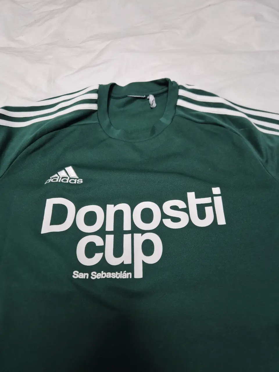 Remera de manga corta verde con el logo de Adidas y la inscripción "Donosti Cup San Sebastián". Ideal para los fanáticos del fútbol y eventos deportivos.