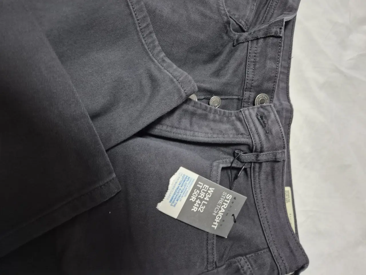 Jeans rectos de hombre, color gris oscuro, con etiqueta de talle visible. Ideal para un look casual y versátil. 34x32