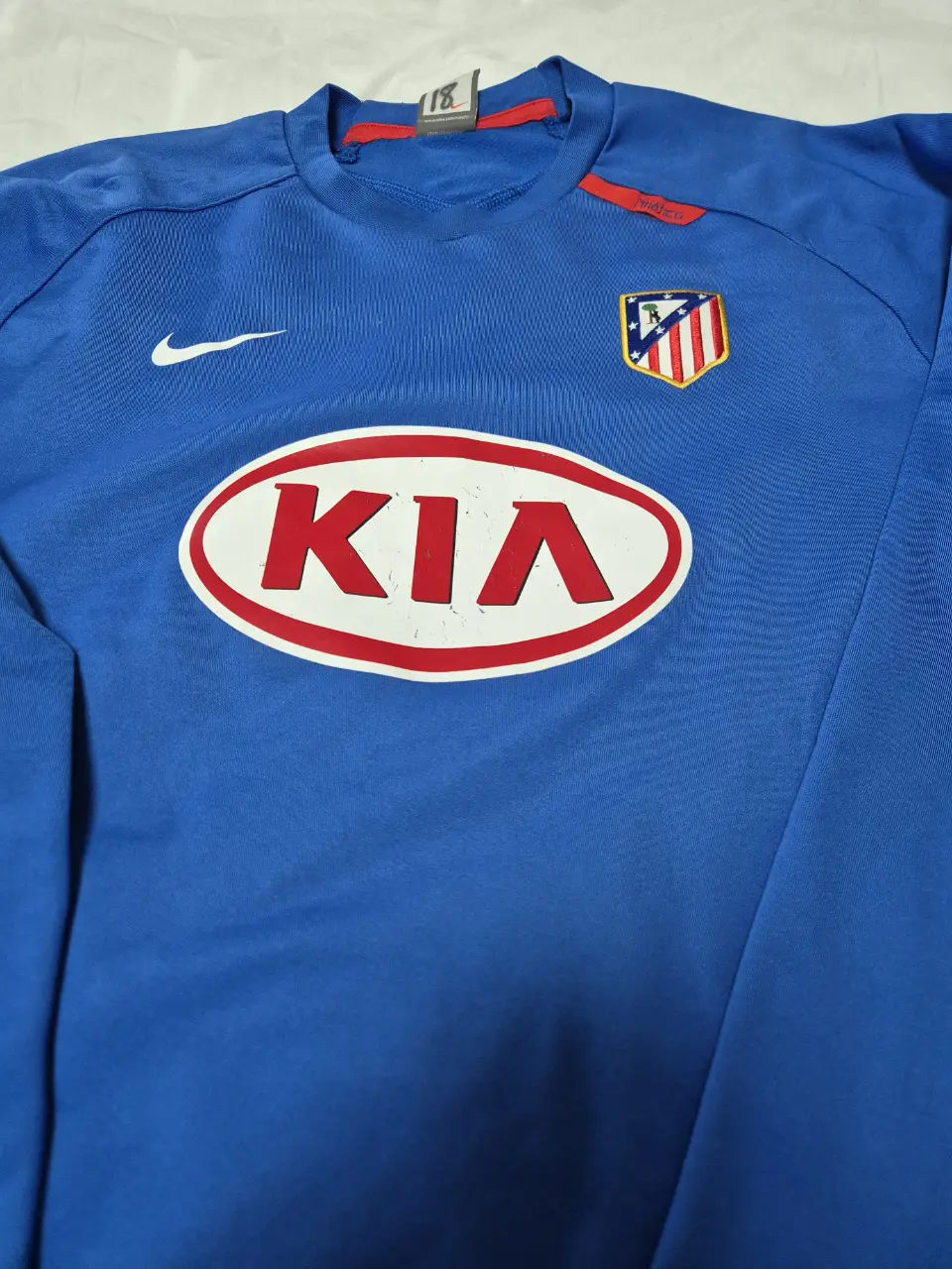 Buzo de manga larga del Atlético de Madrid, dryfit, color azul con detalles en rojo. Cuenta con el logo de Nike y el escudo del equipo, además del logo de KIA. Ideal para coleccionistas del fútbol. Fue usada por Maxi Rodriguez (por eso el número 18 en la etiqueta)