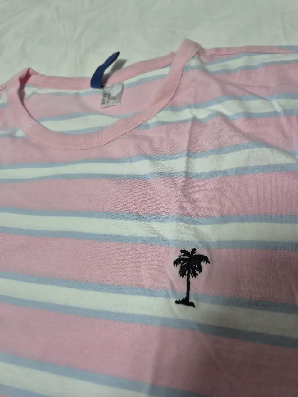 Remera a rayas horizontales en tonos rosa, blanco y celeste. Con un pequeño bordado de palmera en el frente. Ideal para un look casual y fresco.