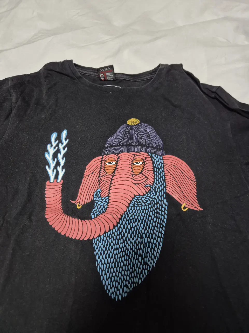 Remera negra de hombre con estampado de un elefante con gorro y barba azul. Diseño original y llamativo, ideal para un look casual y con onda.