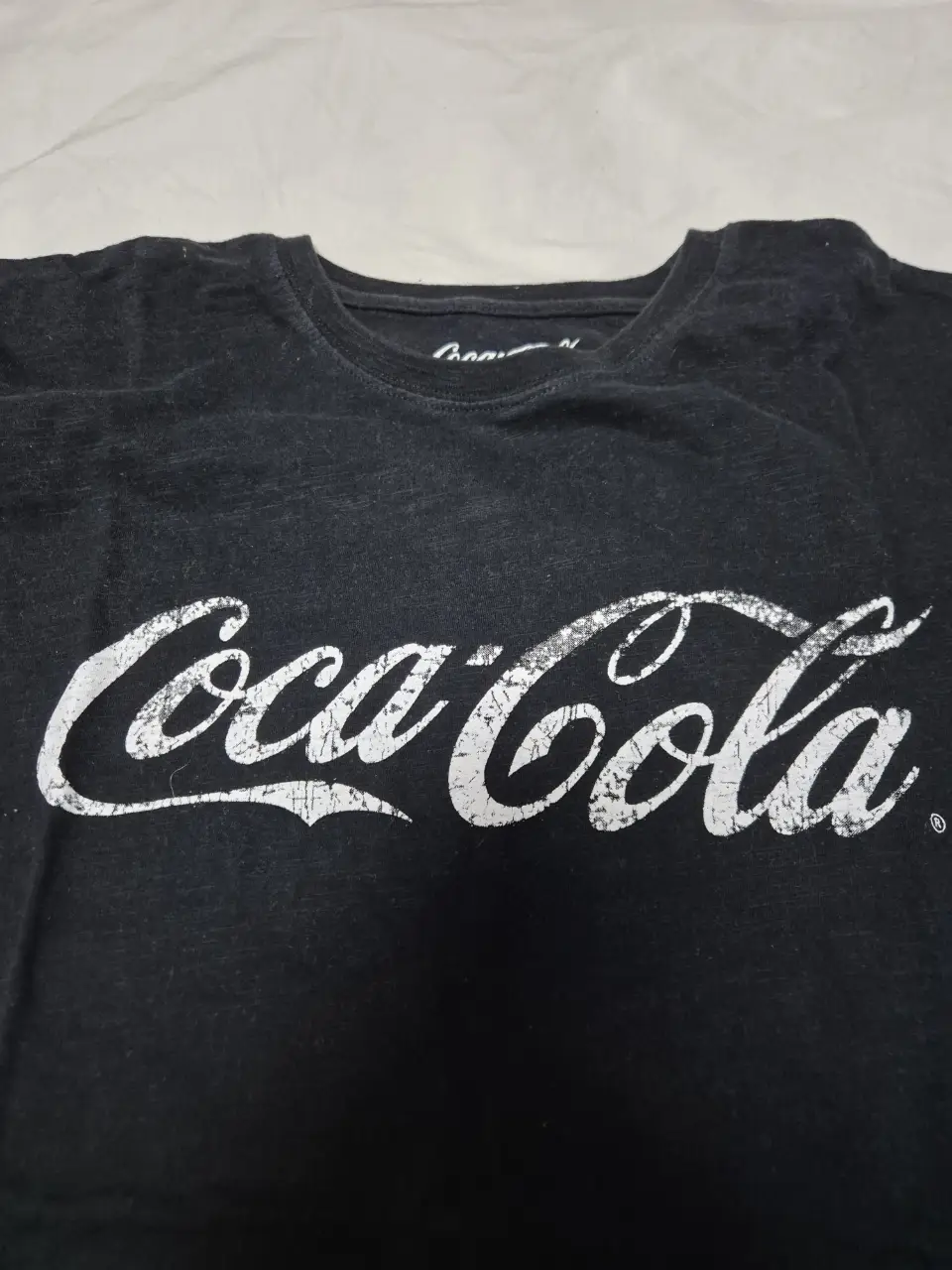 Remera negra de algodón con estampado del logo de Coca-Cola en blanco. Ideal para un look casual y cómodo.