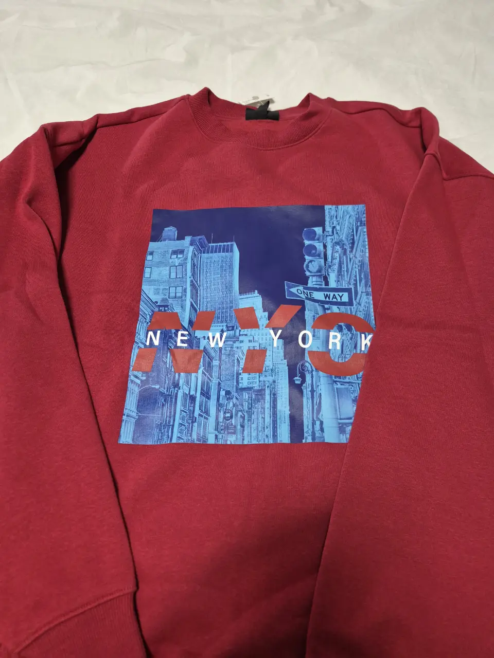 Buzo de cuello redondo rojo con estampado "NYC" en el frente. Diseño urbano con imagen de la ciudad de Nueva York en tonos azules y blancos. Ideal para un look casual y moderno. Es S oversize, a un L chico le queda bien, y a M y S más suelto.