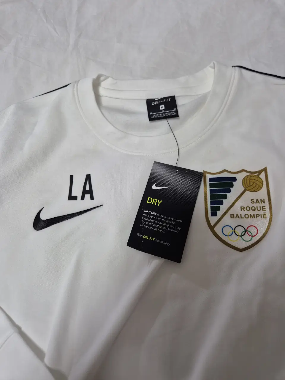 Remera de manga larga Nike Dri-Fit blanca con detalles en negro y logo de LA. Incluye el escudo del equipo San Roque Balompié.