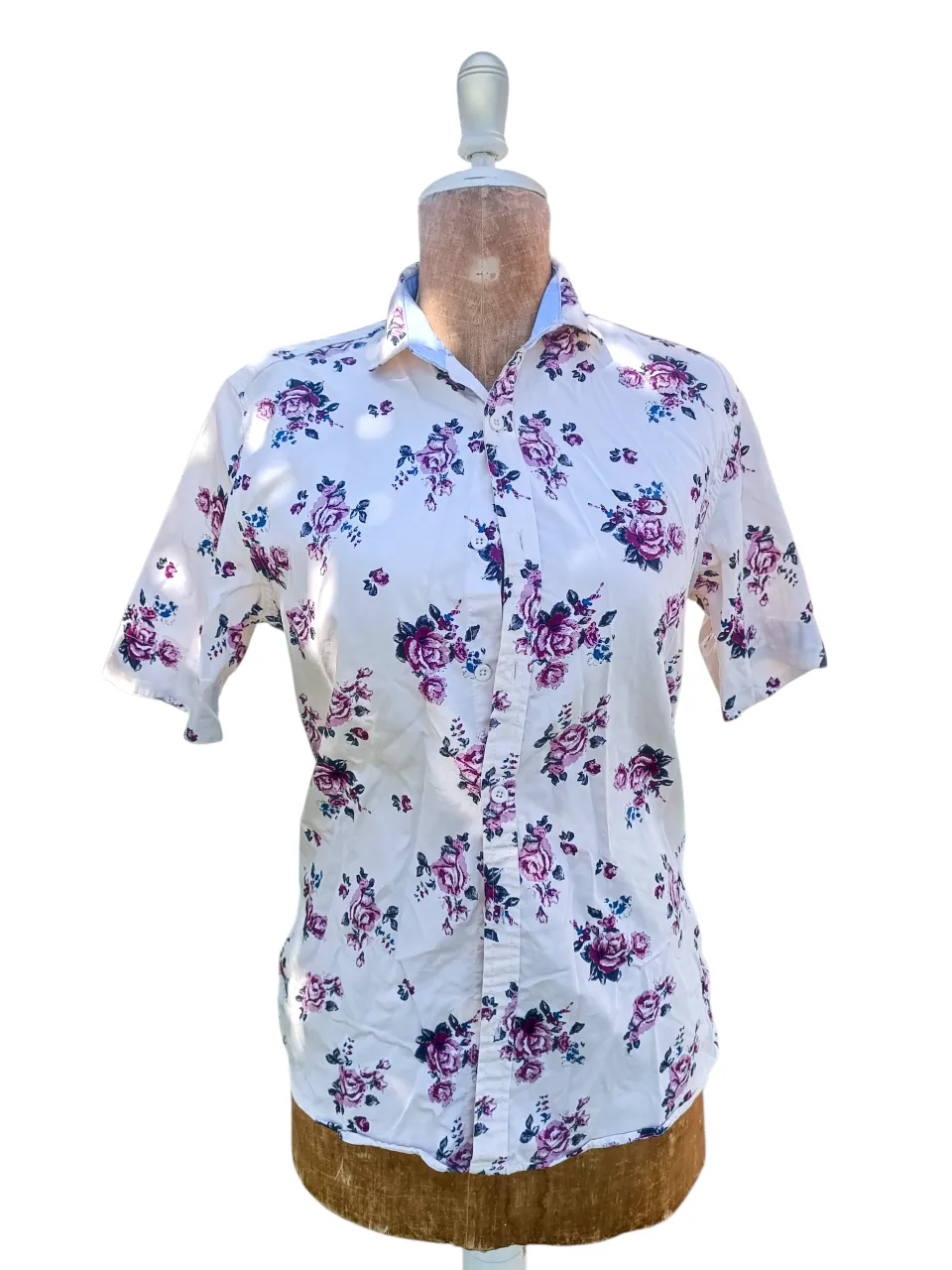 Camisa estampada con flores en tonos violetas y azules sobre fondo blanco. Posee mangas cortas y cuello clásico. Ideal para un look casual y fresco.