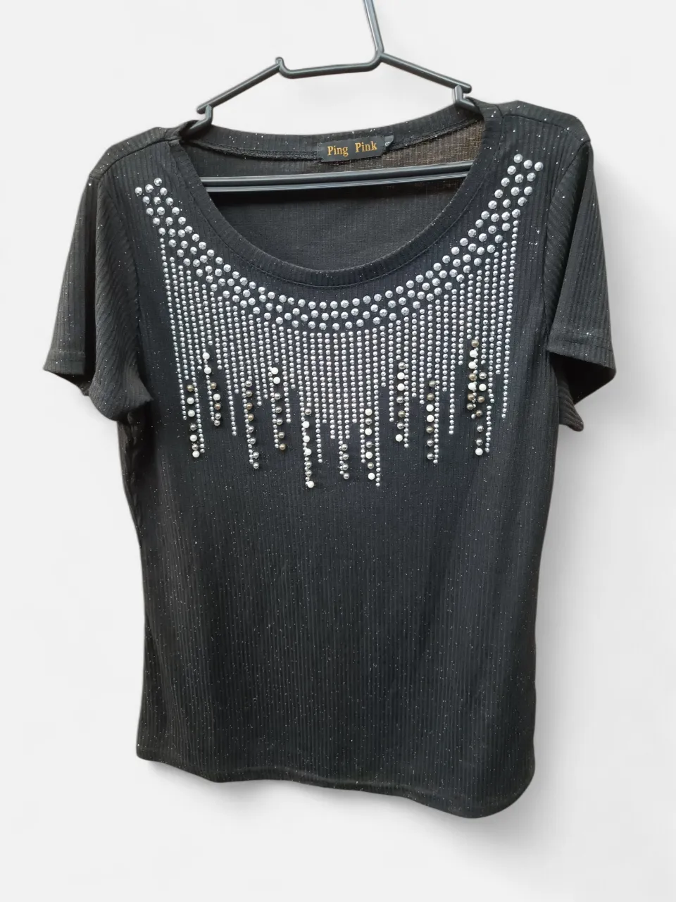 Remera negra con brillos y apliques de strass y perlas en el escote. Diseño único y llamativo, ideal para destacar en cualquier salida.