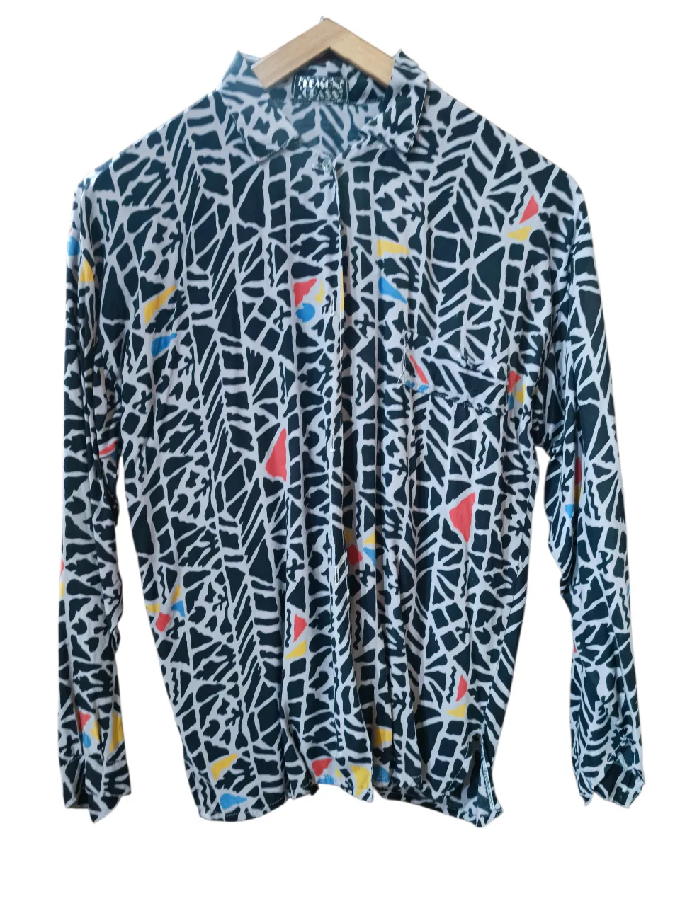 Camisa vintage estampada con un diseño abstracto en blanco y negro, con detalles en rojo, amarillo y azul. Posee cuello camisero, manga larga y un bolsillo falso en el frente.
‼️Prenda vintage. Detalle en la manga, última foto (manchitas blancas).