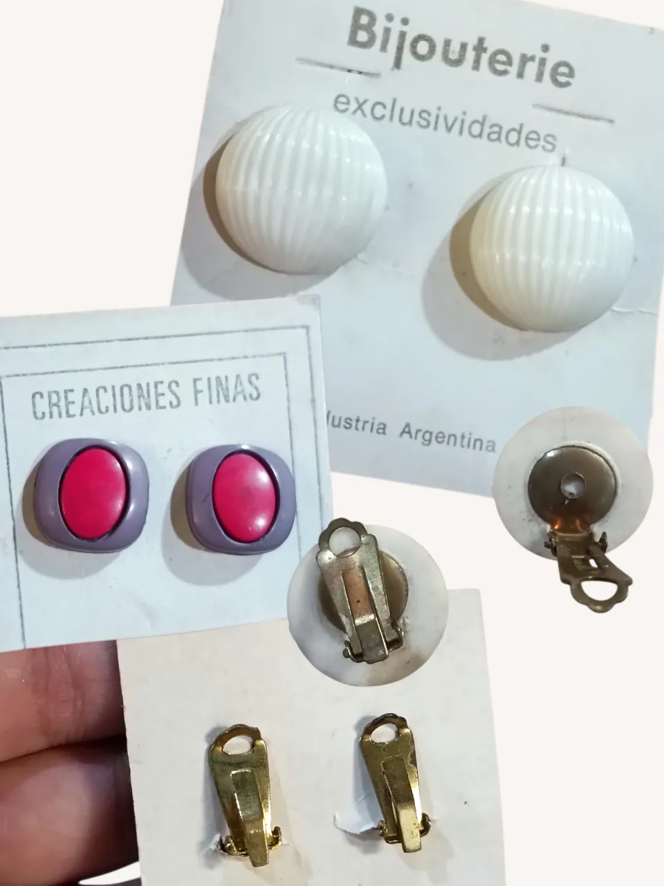 Aros tipo clip con diseño de bolitas acanaladas en blanco. También se incluyen aros tipo clip con diseño ovalado en color rojo y borde violeta grisáceo.