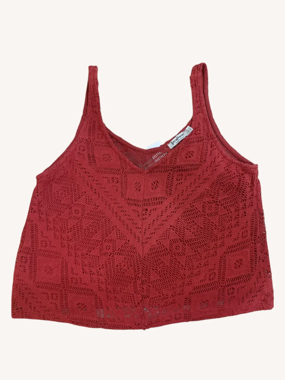 Top tejido de color rojo con detalles de rombos y aberturas. Posee breteles anchos y escote en V.
Tiene forro en la parte delantera y se transluce en la espalda.