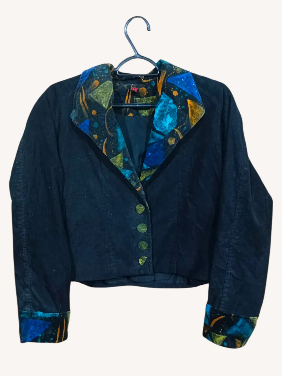 Campera corta de pana negra con cuello y puños de tela estampada con formas geométricas en tonos azul, verde y amarillo. Posee botones al frente. Tiene forro y hombreras.
‼️Falta un botón (el de arriba).