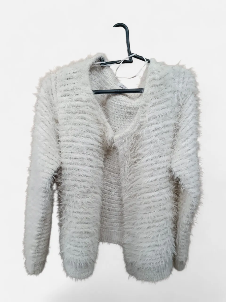 Sweater blanco de tejido suave y peludo, con un diseño de rayas horizontales texturizadas. Posee un escote en V y mangas largas. Ideal para un look abrigado y con estilo.