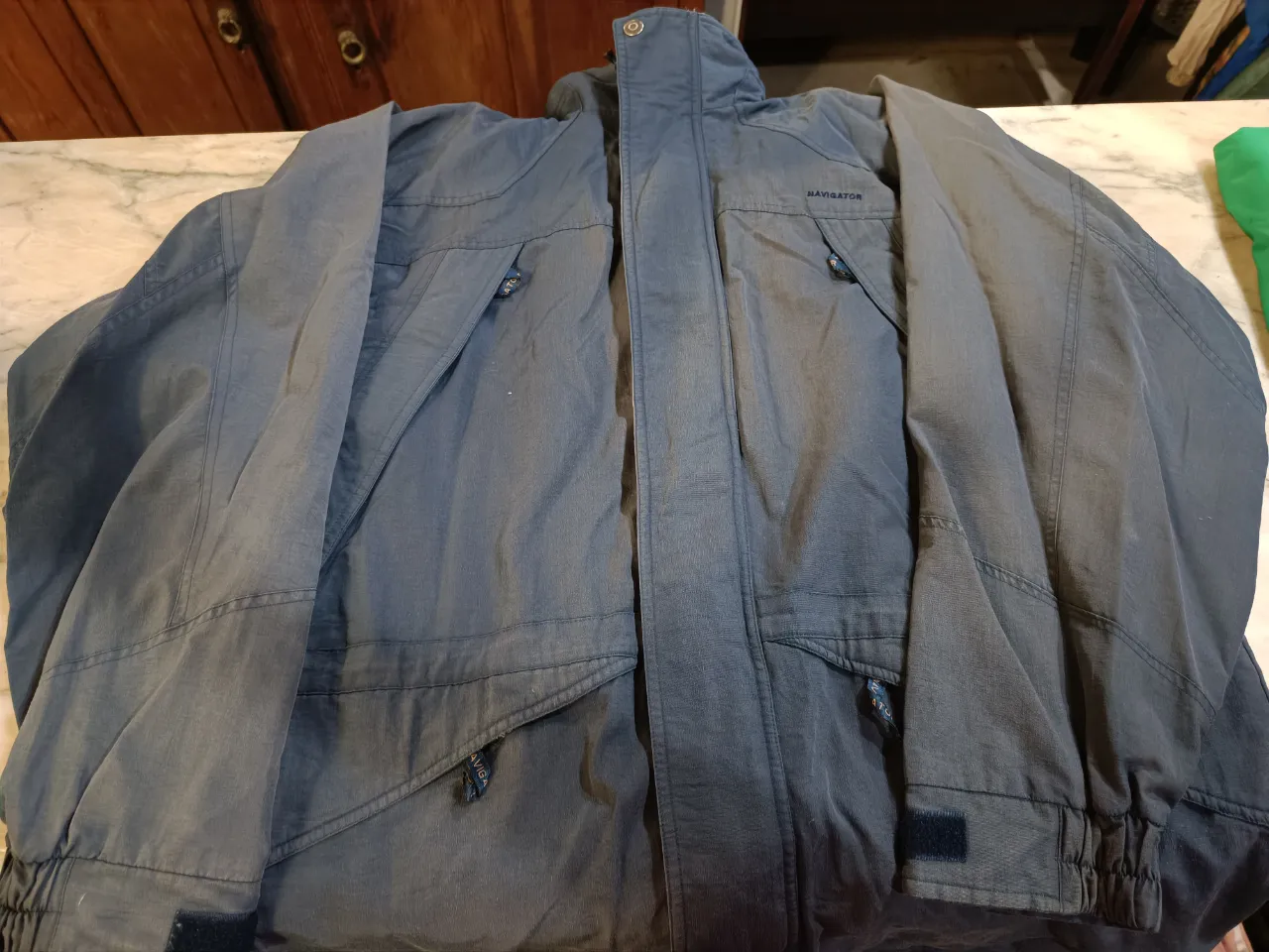 Campera azul marino con cuello alto y cierre. Posee bolsillos frontales con cierre y solapa, y un bolsillo interno con cierre. La marca 'NAVIGATOR' se encuentra visible en el cuello y en un bolsillo.
📏 Ancho 71 cm. Sisa 30 cm. Largo 85 cm.
‼️Tiene los elásticos del borde inferior vencidos y algunos descocidos en el forro. 