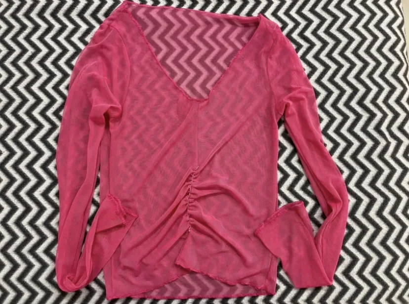 Remera manga larga de red, color fucsia, con escote en V y detalles de fruncido en el frente. Ideal para un look canchero y moderno.