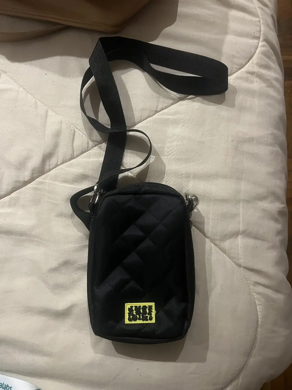 Bandolera negra acolchada con logo amarillo. Ideal para llevar lo esencial con estilo.