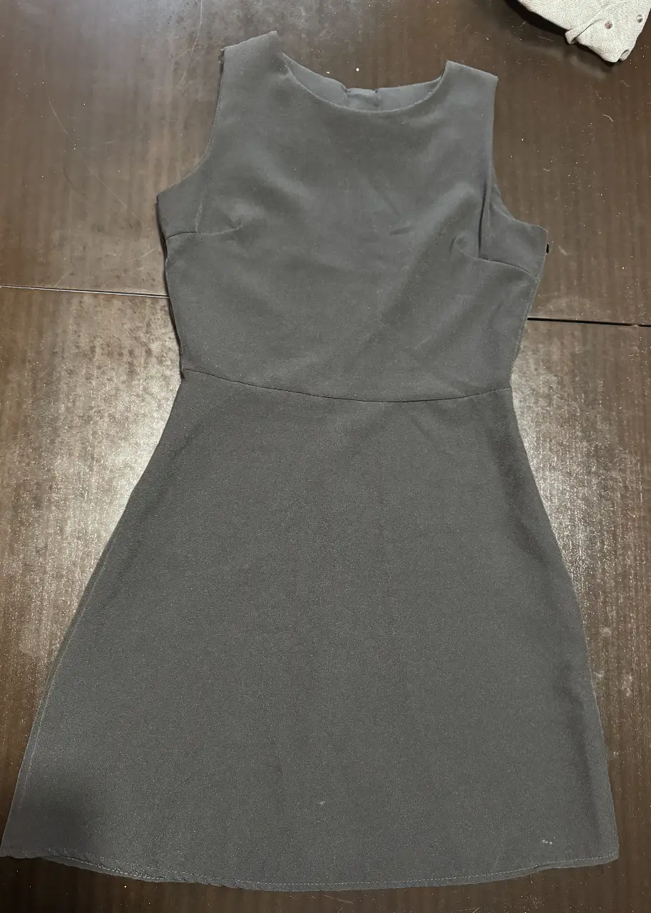Vestido negro mini, sin mangas, con corte en la cintura y falda con vuelo. Ideal para una salida o evento formal.