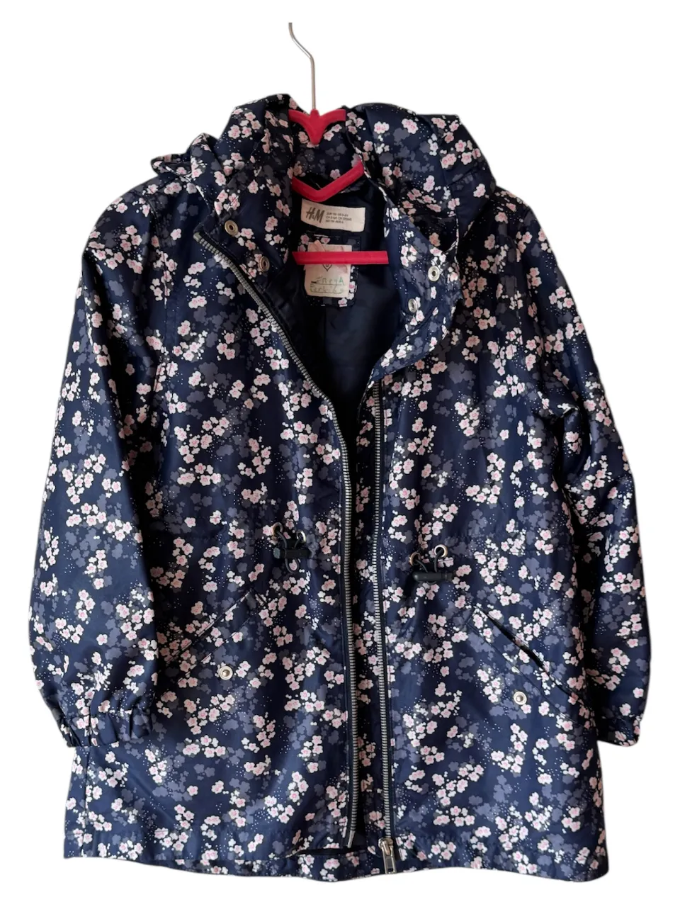 Campera impermeable para niña, con estampado floral en tonos azul marino y rosa. Cuenta con capucha, cierre y bolsillos. Ideal para proteger a tu hija de la lluvia con estilo.