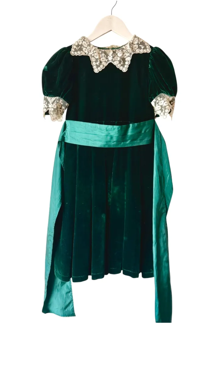 Vestido inglés tipo terciopelo verde con cuello y puños de encaje blanco. Posee un lazo ancho de satén verde en la cintura.