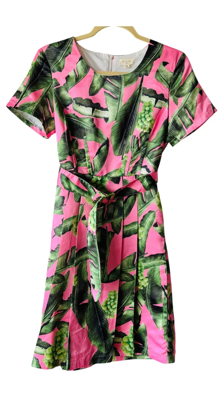 Vestido midi de mujer con estampado de hojas tropicales en tonos rosa y verde. Confeccionado en tela ligera, presenta un diseño con cinturón para ajustar la cintura y realzar la figura. Ideal para un look fresco y moderno.