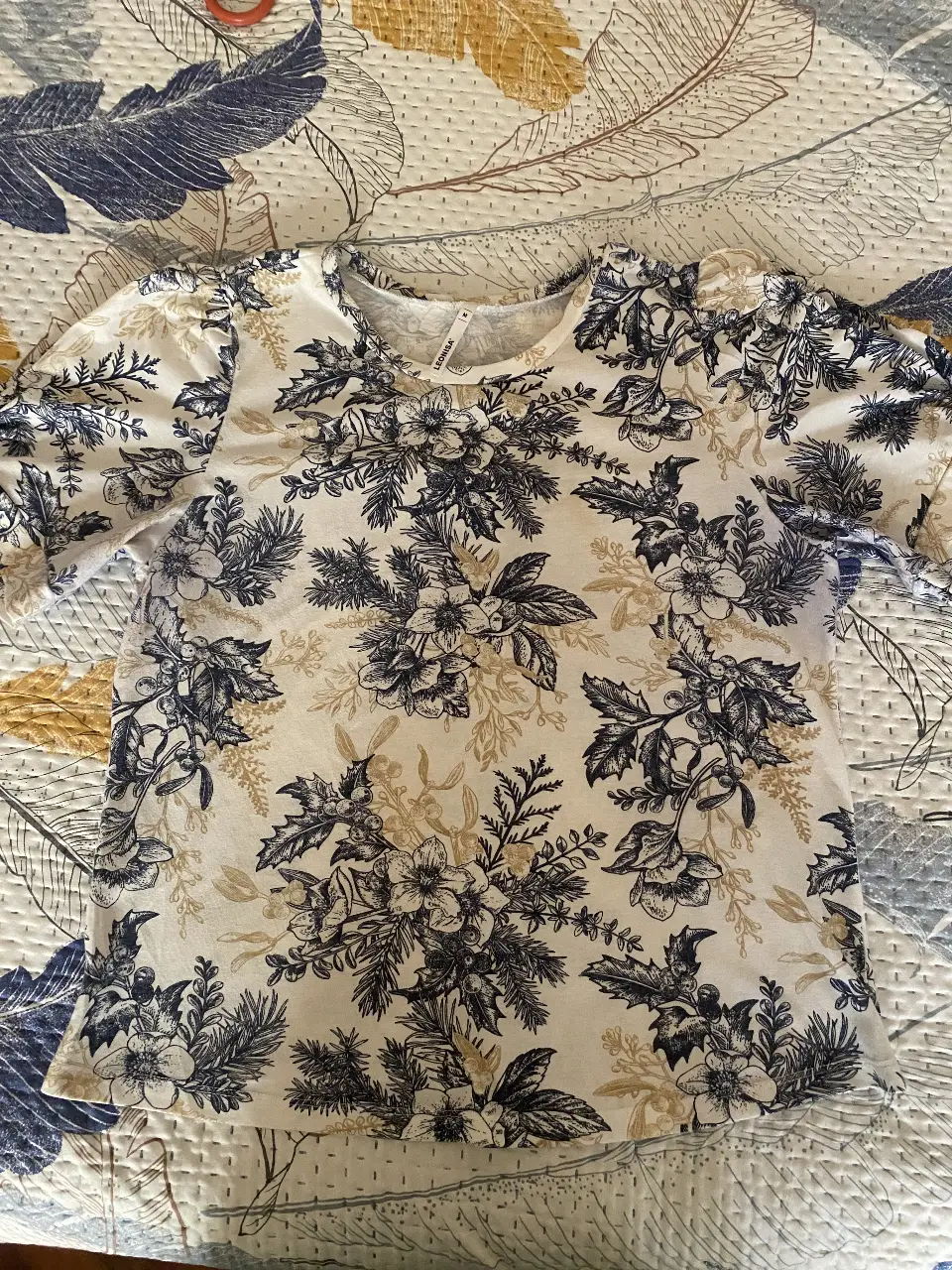 Blusa de mujer con estampado floral en tonos blanco y azul. Manga 3/4 con detalle de fruncido en el hombro. Cuello redondo. Ideal para un look casual y fresco.