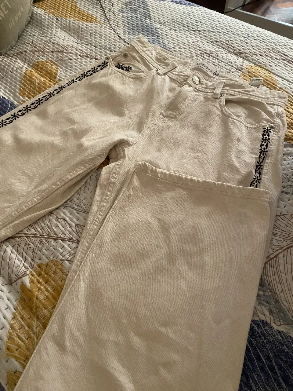 Jeans rectos color crudo con detalles bordados en negro en los laterales y en el bolsillo. Talle 38, de la marca Stradivarius. Ideal para un look casual y moderno.