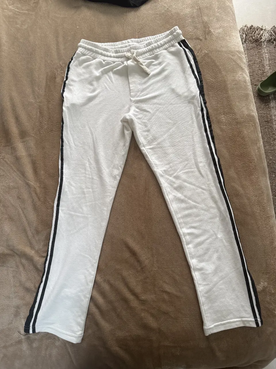 Pantalón deportivo blanco con franjas negras laterales. Ideal para un look casual y cómodo.