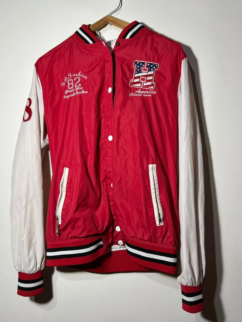 Campera bomber roja con mangas blancas y detalles en negro. Estilo deportivo y casual, ideal para un look urbano y canchero. Con capucha y cierre frontal.