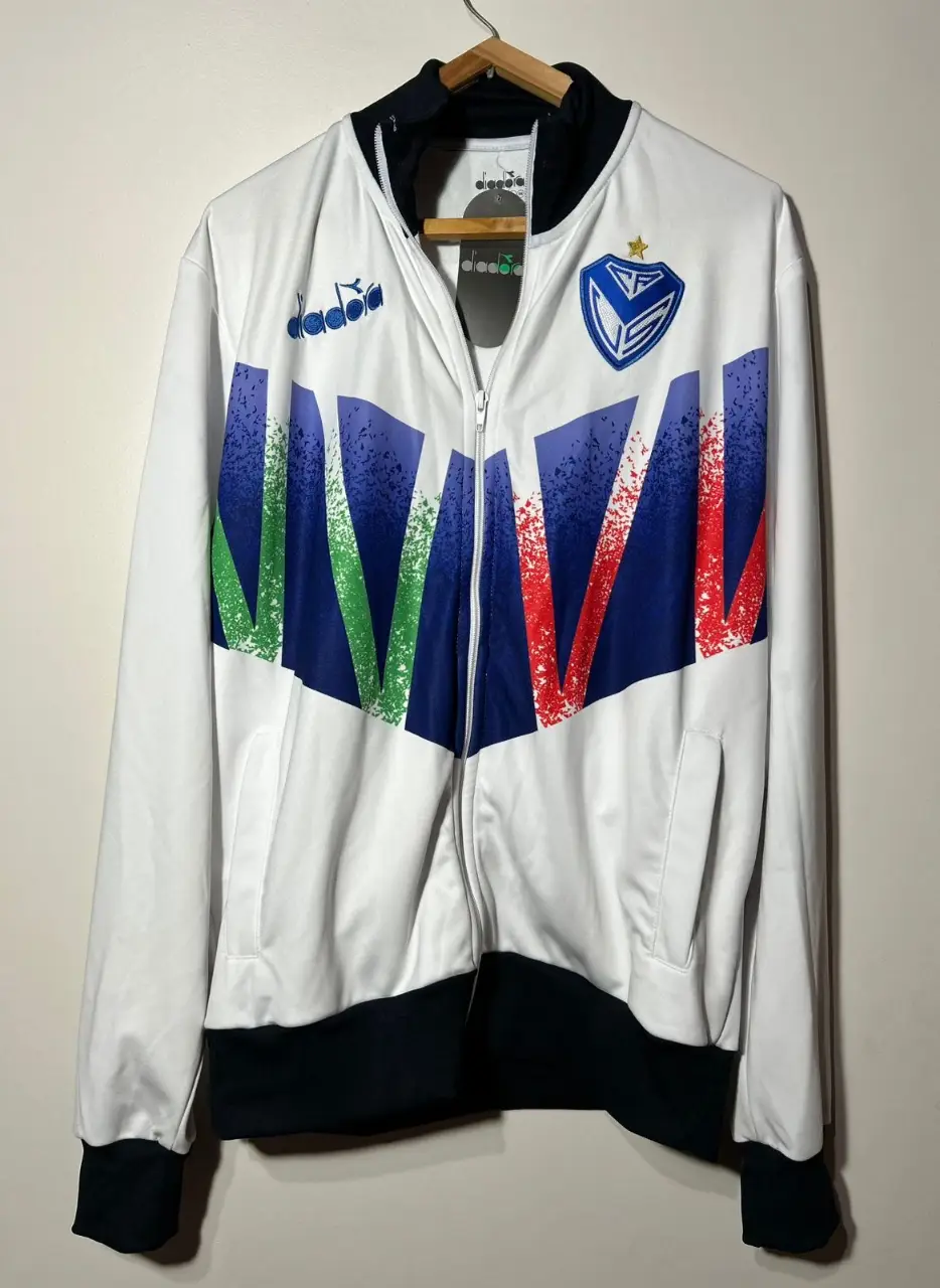 Campera deportiva con cierre Diadora del club Vélez Sarsfield, con cierre y detalles en azul, verde y rojo. Ideal para fanáticos del fútbol y para usar en ocasiones casuales.