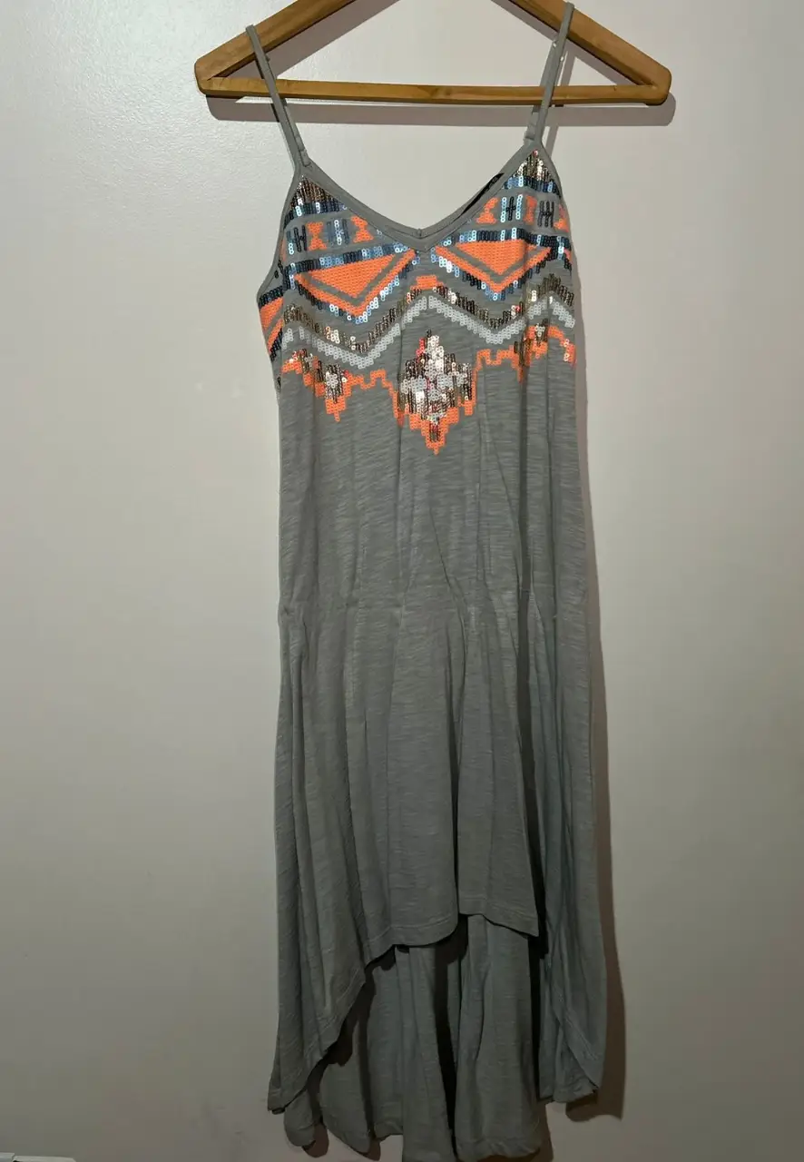 Vestido mini gris con la parte trasera más larga con detalles bordados en la parte superior. Ideal para un look casual y fresco.Importado