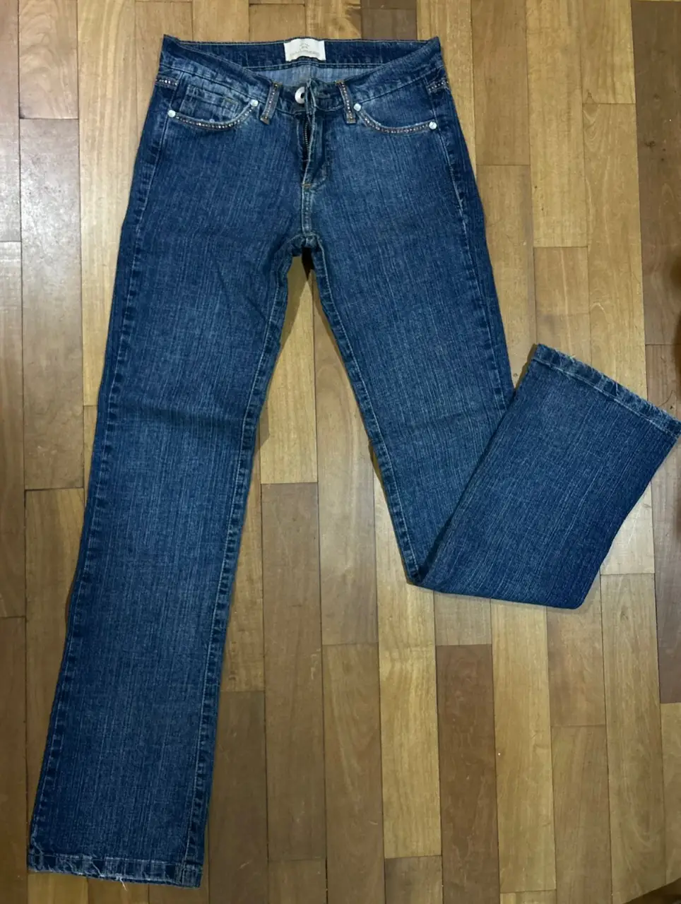 Jeans de mujer, tiro medio, con detalles de strass en los bolsillos delanteros y traseros. Corte recto con un ligero acampanado en la bota. Marca Sarkany Jeans. Talle 24.Detalles con brillos dorados en la parte delantera de bolsillos trabas de cinturón y parte trasera