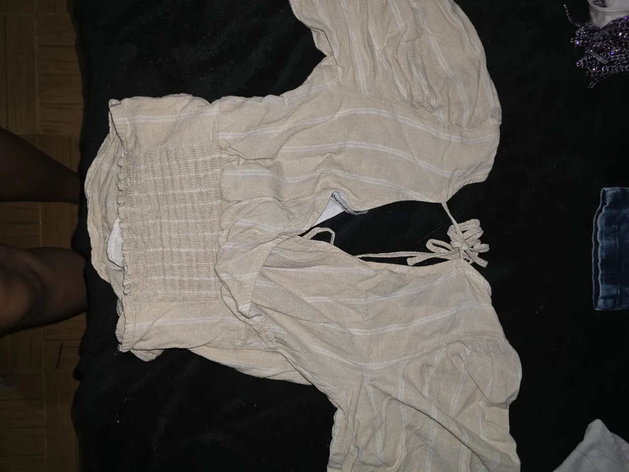 Blusa de lino color tiza con rayas finas blancas. Posee mangas cortas abullonadas y escote cruzado con lazo en la espalda. La parte inferior es elastizada para un mejor ajuste.