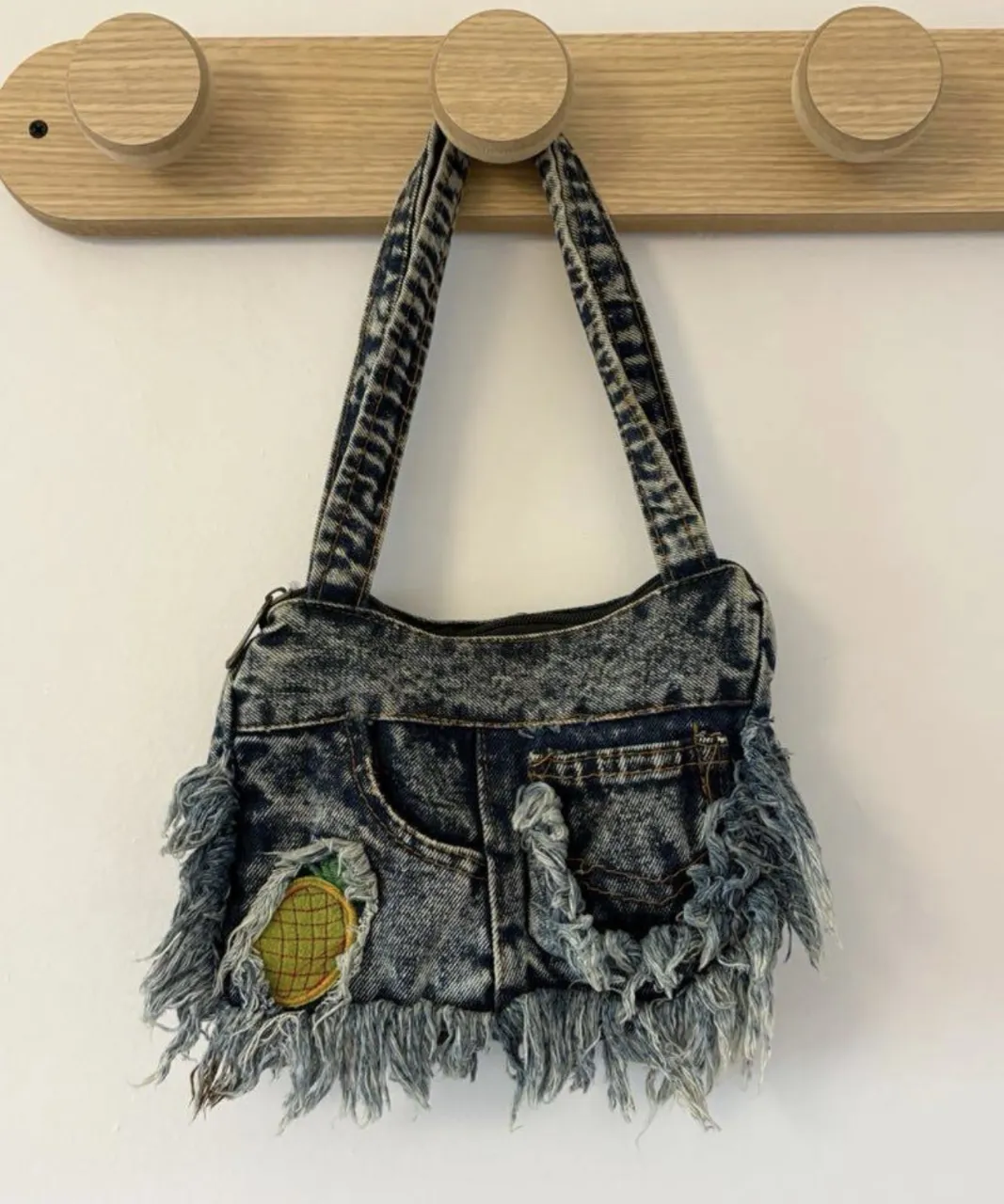 mini cartera de jean azul lavado con flecos deshilachados y un parche de piña. 
medida 21 x 17cm