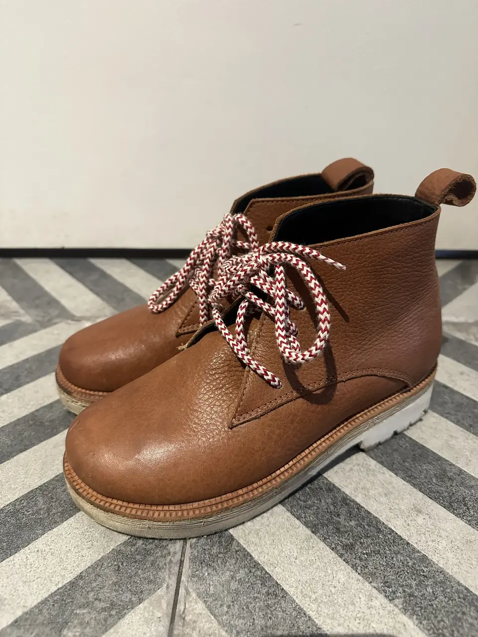 Botines de cuero marrón con cordones bicolor rojo y blanco. Suela blanca con detalles marrones. Ideales para un look casual y moderno.