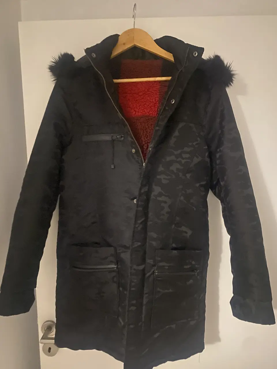 Campera larga negra con estampado camuflado, capucha con piel sintética y forro interior rojo. Ideal para el invierno.