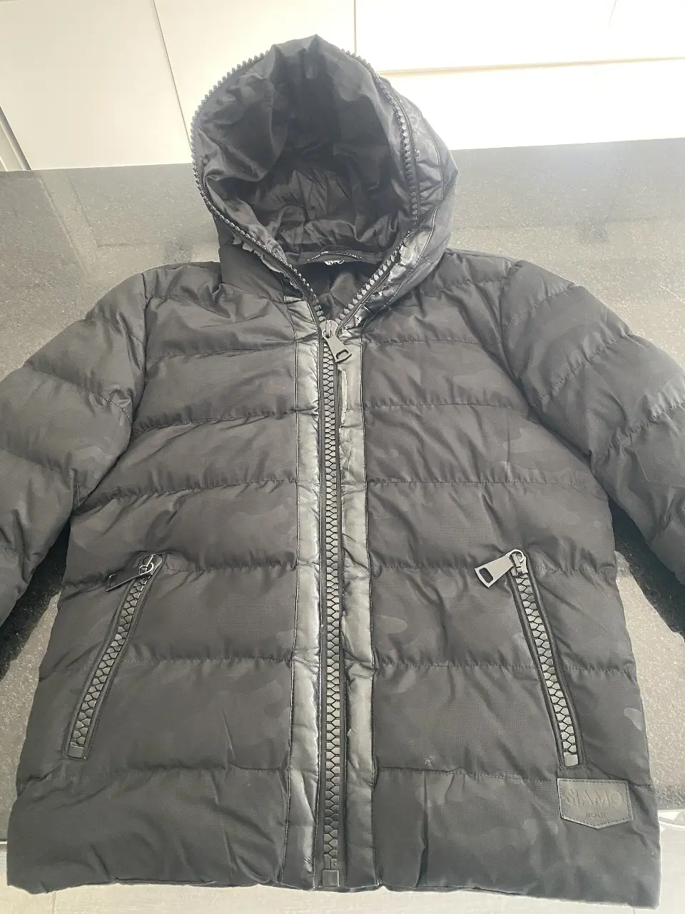 Campera de pluma negra para hombre, con capucha y cierre. Ideal para el invierno, con un diseño acolchado y bolsillos con cierre.