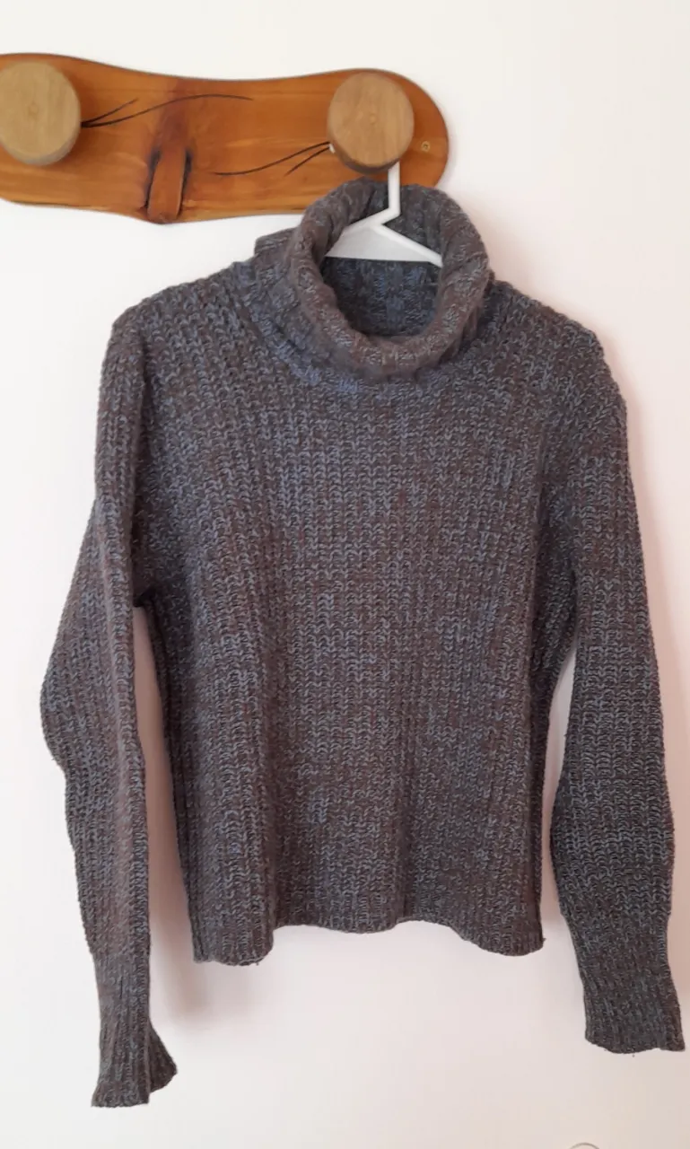 Sweater de lana tejido con cuello alto y mangas largas. Presenta un diseño de tejido en espiga con hilos en tono azulado y marrón. Posee un detalle de etiqueta redonda de cuero con un árbol grabado en una de las mangas. De lana mohair. Marca Telares del Bosque. Muy abrigado. 