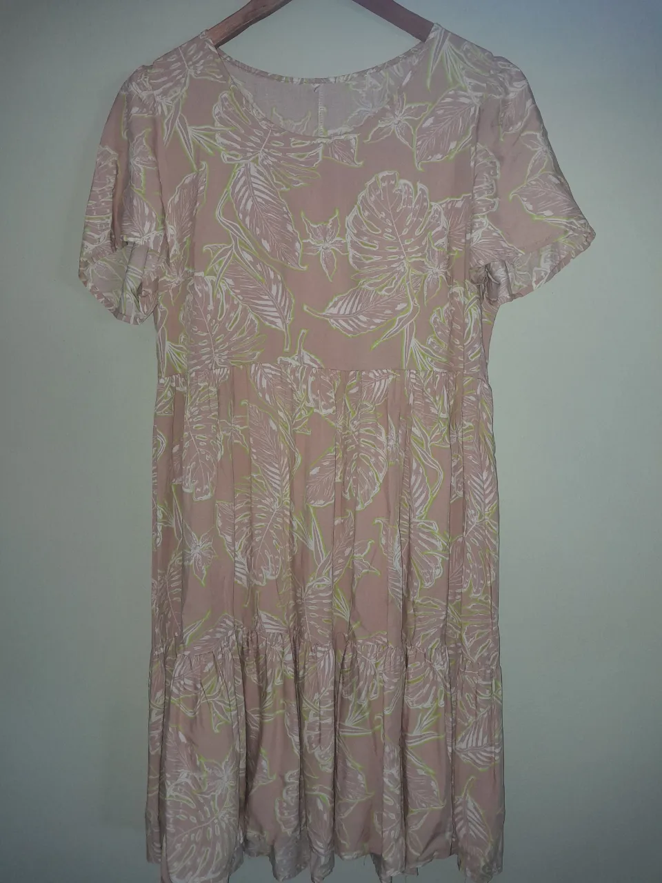 Vestido rosa con estampado de hojas tropicales en blanco y verde lima. Posee mangas cortas y volados en la parte inferior.