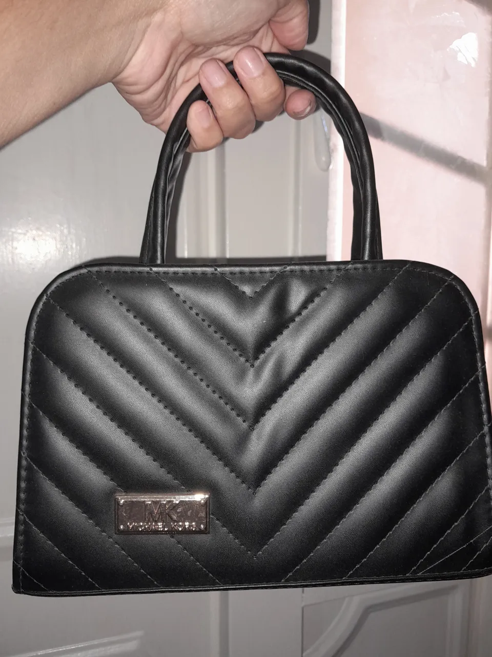 Bolso negro matelaseado con manijas cortas y logo metálico de la marca en el frente.