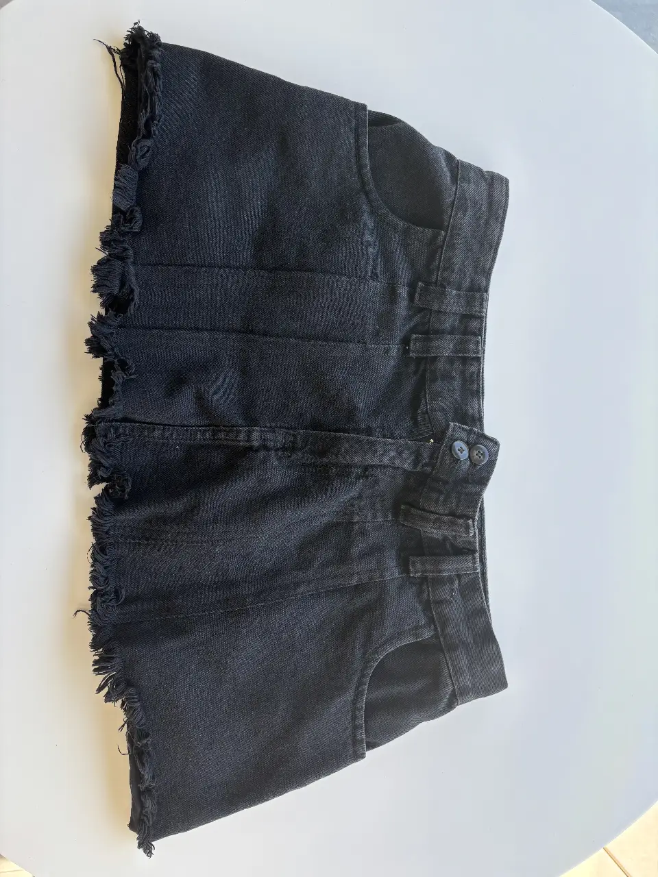Pollera de jean negro con terminación desflecada. Tiro bajo, ideal para un look casual y moderno. Perfecto para combinar con remeras y tops.