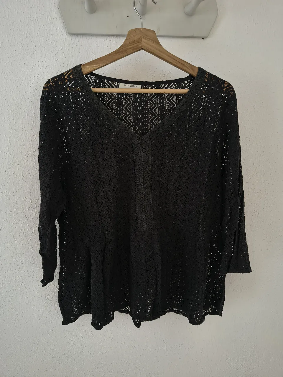 Blusa negra de encaje con mangas 3/4 y escote en V. Diseño delicado y romántico, ideal para un look elegante o casual.