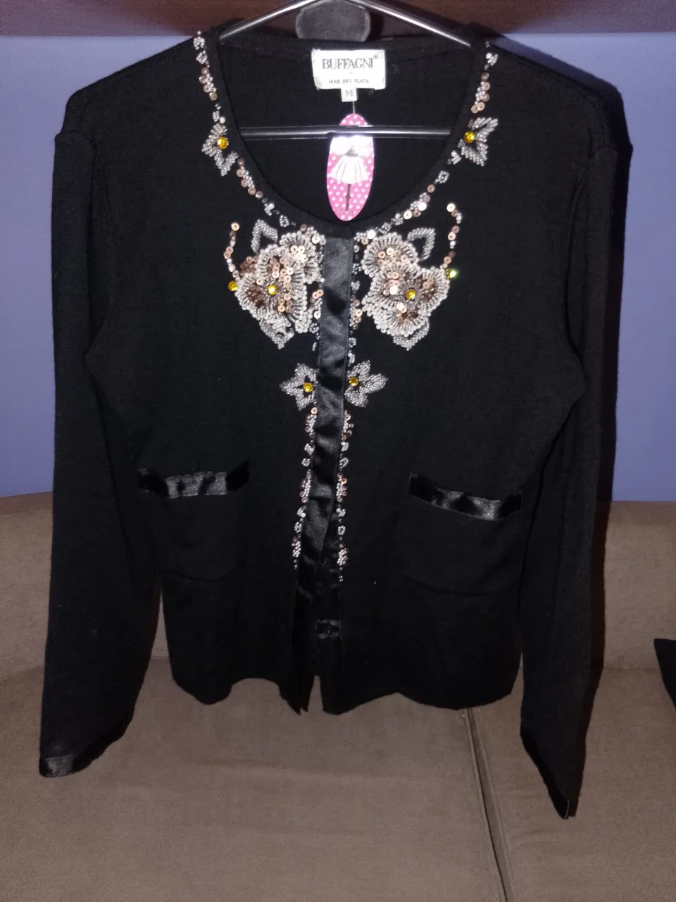 Cardigan negro de la marca Buffagni, con detalles bordados y apliques en la parte delantera. Posee dos bolsillos frontales y cierre con botones. Ideal para un look elegante y sofisticado.