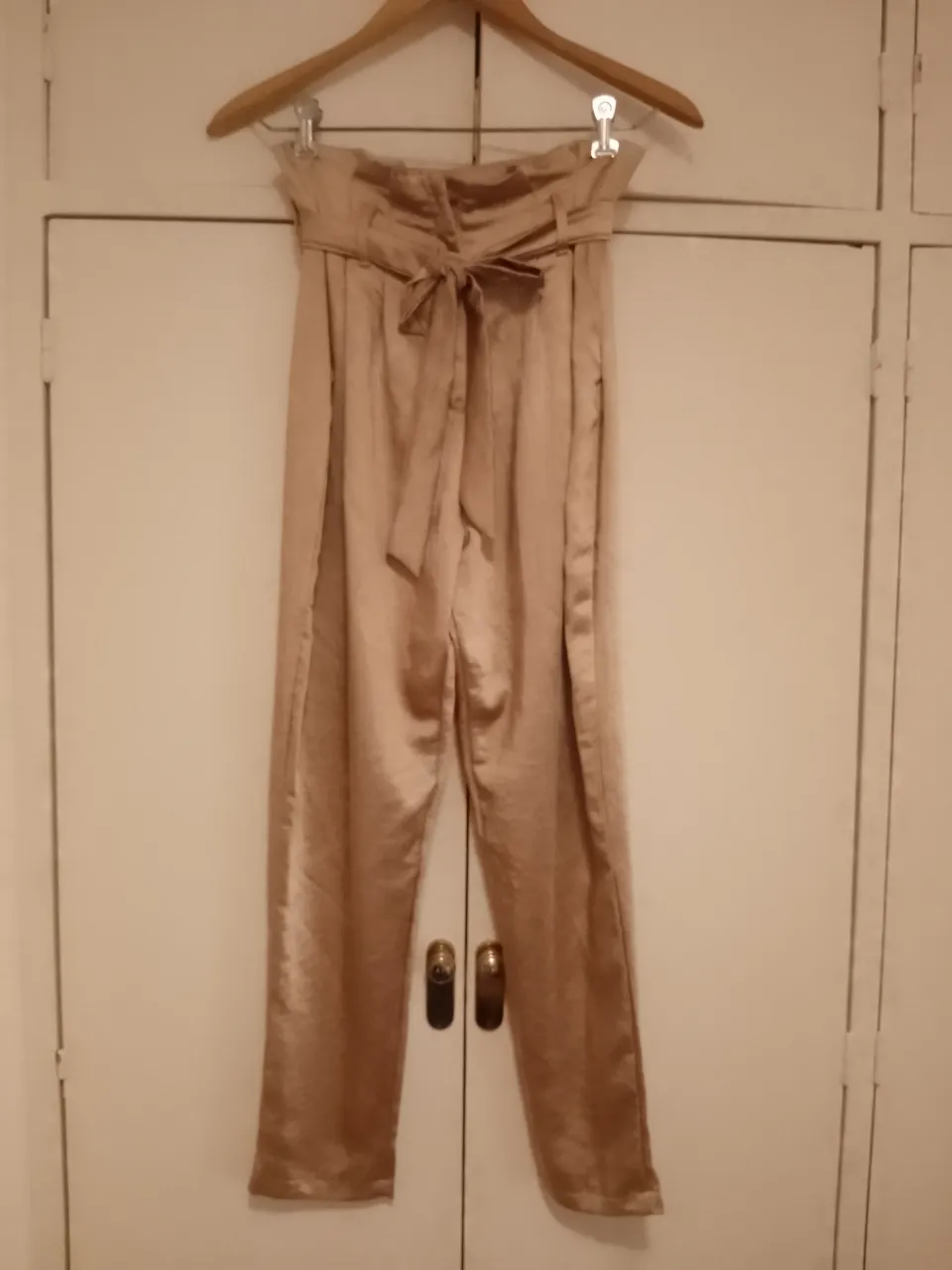 Pantalón largo de seda color champagne con lazo en la cintura. Posee pretina ancha y bolsillos laterales.