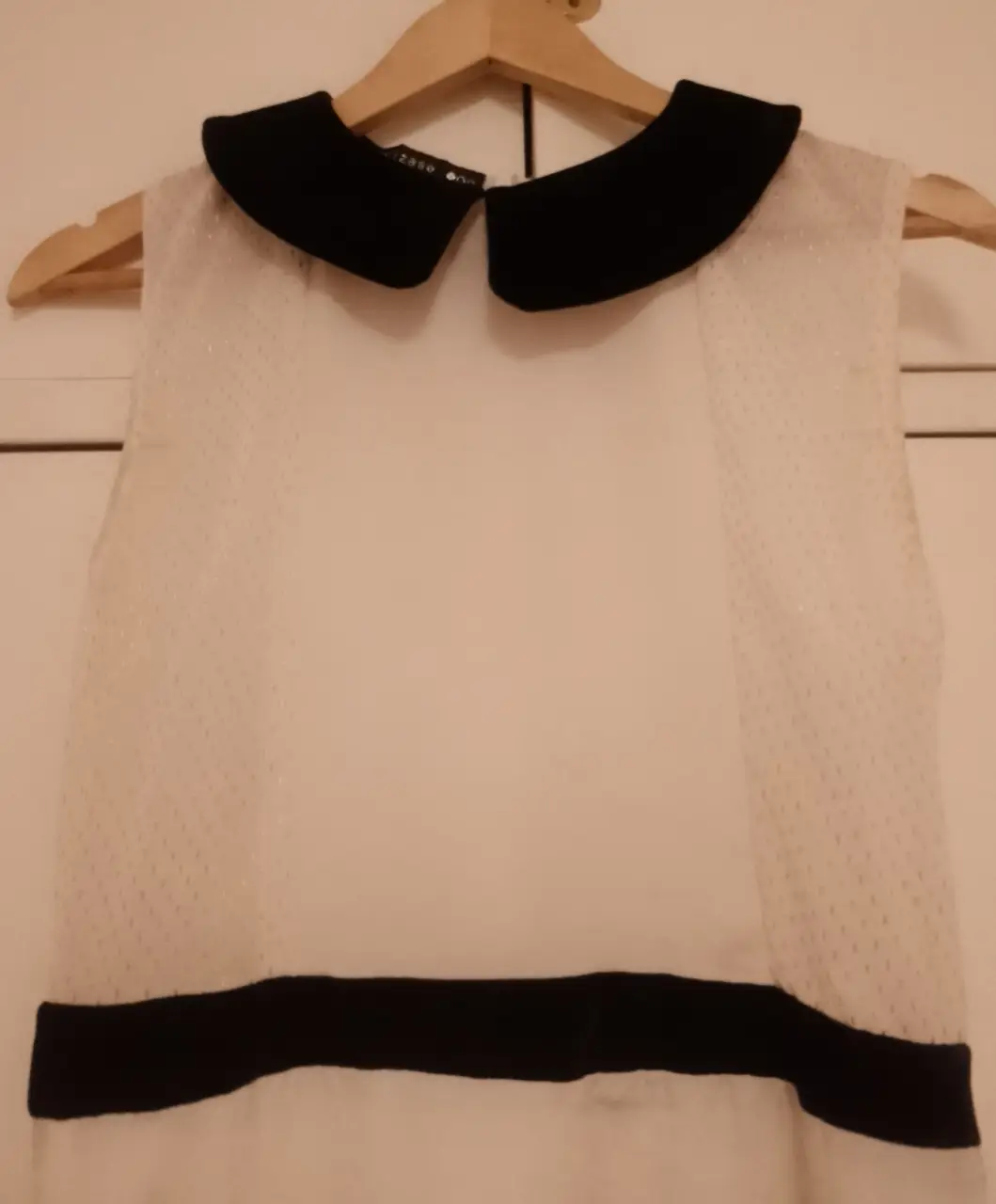 Vestido midi blanco con cuello Peter Pan negro y detalle de cinta negra en la cintura. Ideal para un look elegante y femenino.