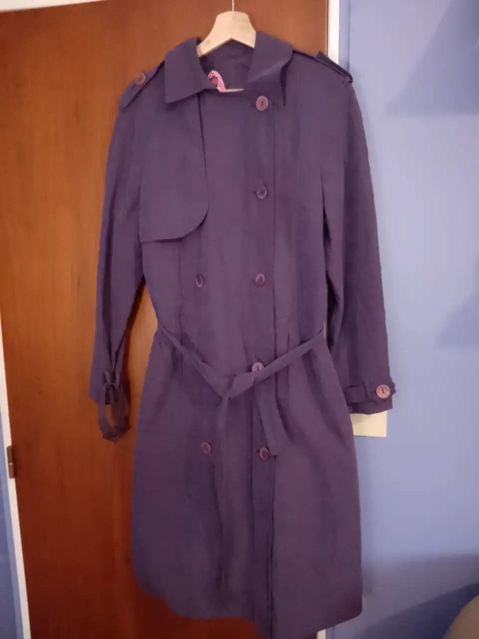 Trench coat de color violeta, con cinturón para ajustar en la cintura. Posee botones y detalles en los hombros y puños. Ideal para un look elegante y sofisticado.