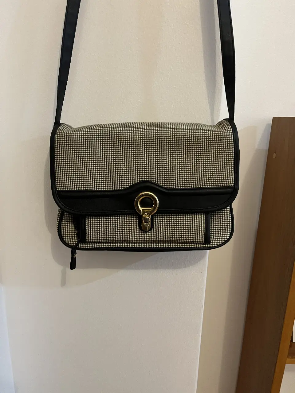 Bandolera vintage con estampado de pata de gallo en blanco y negro. Detalles en negro, incluyendo la correa ajustable y el cierre. Interior espacioso con múltiples compartimentos. Tiene una pequeña manchita blanca (ver ultima foto)