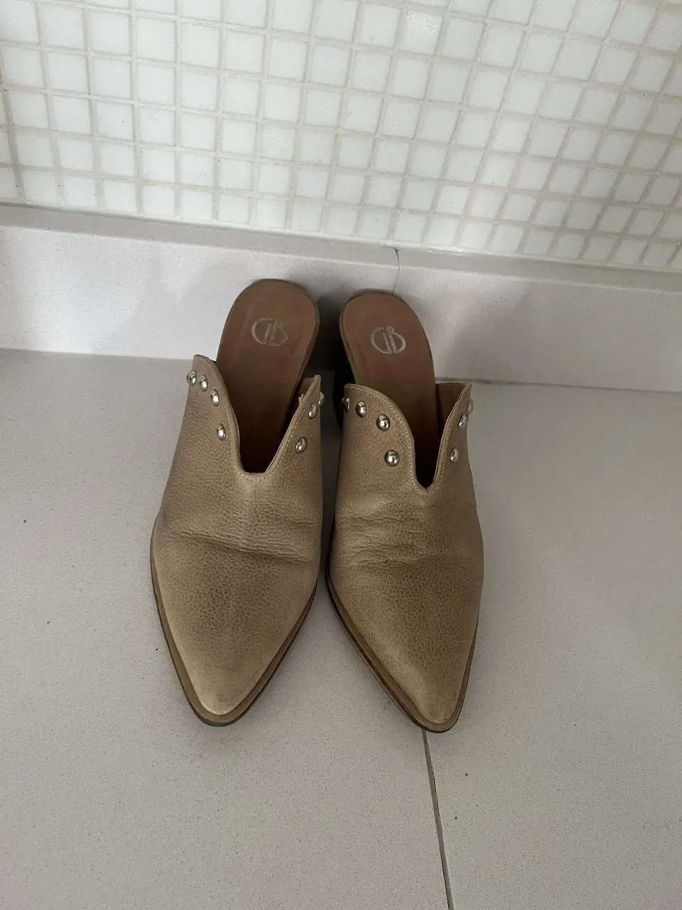 Mules de cuero color crudo con detalles de tachas plateadas. Diseño elegante y versátil, ideales para complementar cualquier look.