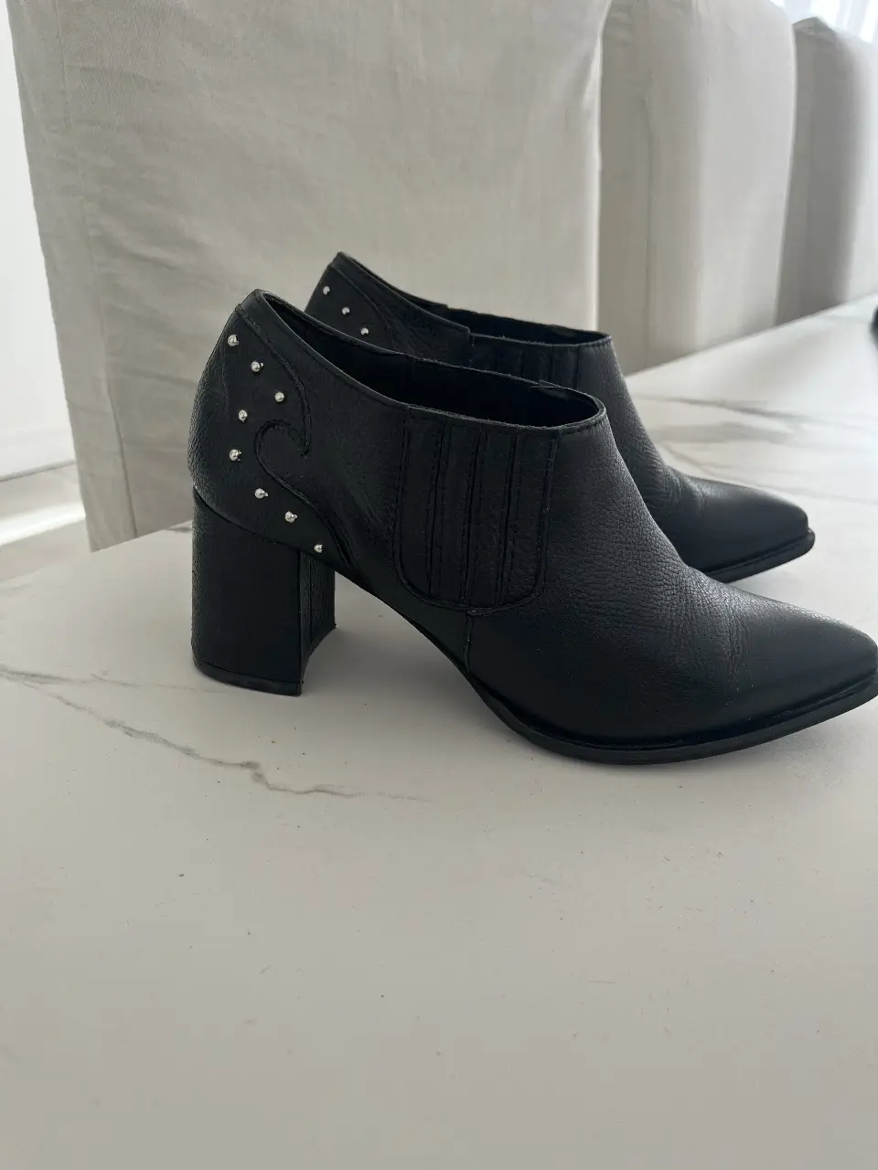 Botines negros de cuero con detalles de tachas plateadas. Diseño elegante con punta fina y taco cuadrado. Ideales para un look moderno y sofisticado.
